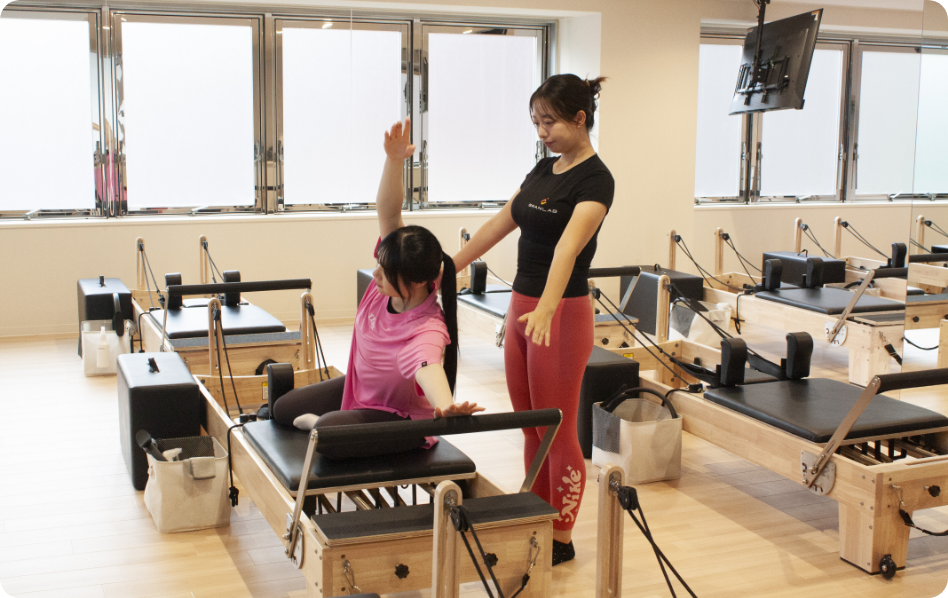 トレーナーの指導を受けてピラティスを体験する女性