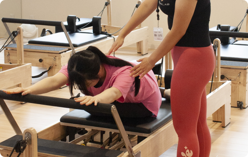 トレーナーの補助を受けてピラティスを体験する女性