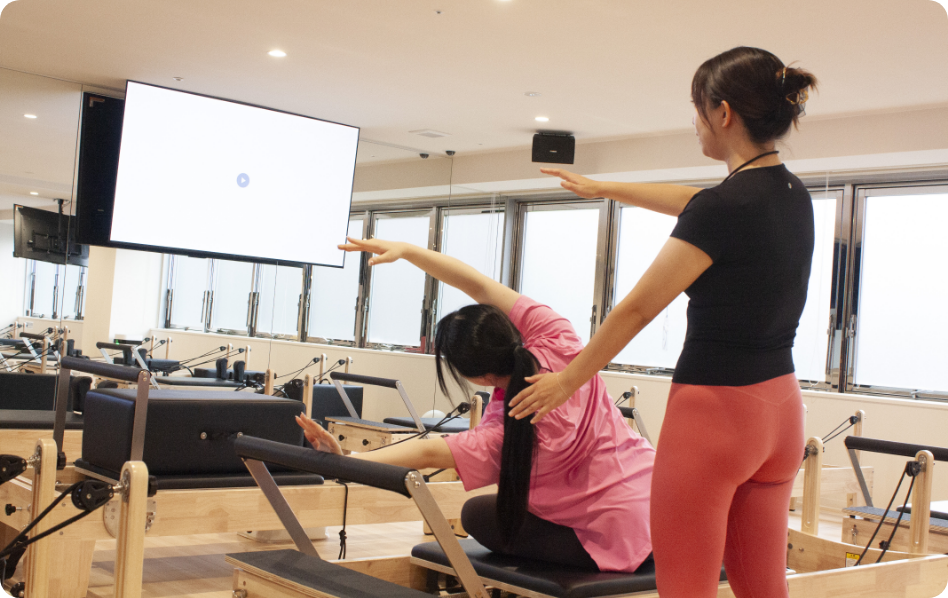 トレーナーの補助を受けながらピラティスを体験する女性